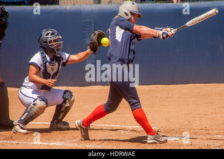 Fino a bat, un collegio di donna softball player altalene a sfera e manca ad un gioco sul campo in Fullerton, CA. Nota batting casco e catcher cattura la palla. Foto Stock