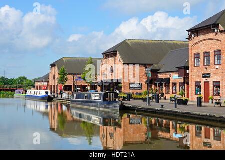 Narrowboats ormeggiati davanti a bar, negozi e ristoranti nel bacino del canale, Barton-sotto-Needwood, Staffordshire, England, Regno Unito Foto Stock