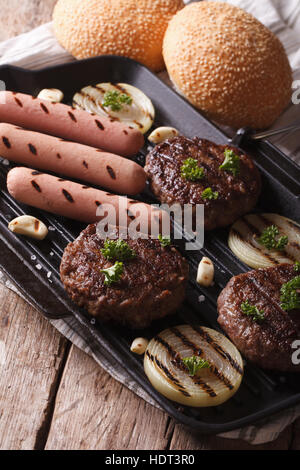 Hamburger e salsicce con verdure su una padella per grigliare closeup. In verticale Foto Stock