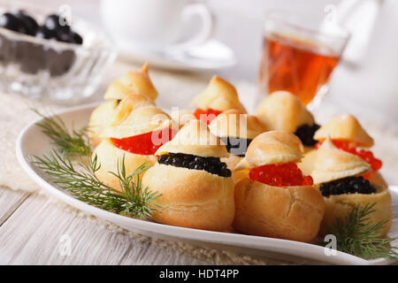 Profiteroles riempito con rosso e caviale nero su una piastra di close-up orizzontale. Foto Stock