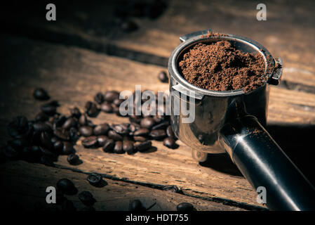 Il caffè macinato nel filtro porta supporto sulla superficie di legno con i fagioli è sceso in modo lasco Foto Stock