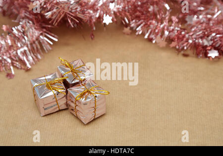 Sfondo di natale con decorazioni rosa tinsel e confezioni regalo su carta naturale Foto Stock