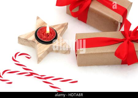 Regali di natale con centine rosso e nastri accanto ad una candela e candy canes contro uno sfondo bianco Foto Stock