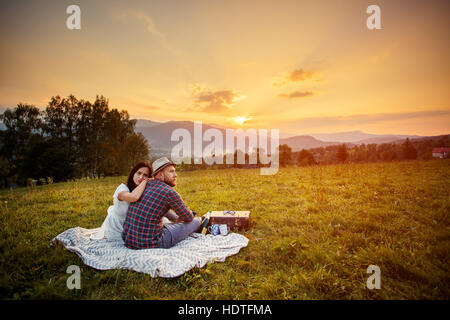 Matura in amore su bianco plaid. sfondo tramonto sulle montagne Foto Stock