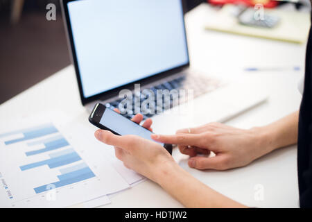 Donna con le mani in mano utilizzando il telefono cellulare e il computer portatile in ufficio Foto Stock