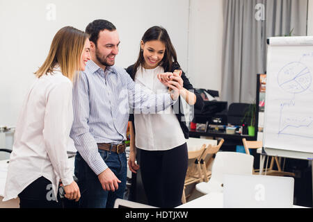 Il gruppo di quattro diversi allegro co-lavoratori tenendo ritratto di auto e rendere divertente gesti con le mani a small office Foto Stock