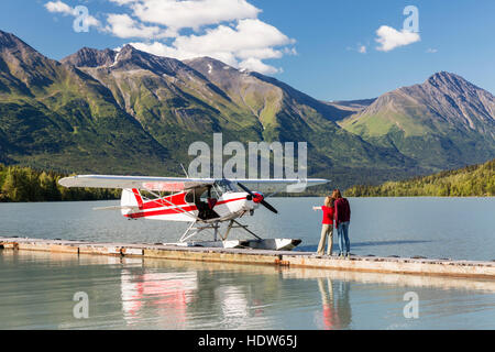 Una madre con sua figlia che guarda Un aereo galleggiante ancorato alla Trail Lake Float Plane base in Un giorno limpido, le montagne Kenai in background... Foto Stock