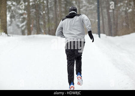 Uomo che corre su strade coperte di neve in inverno road nella foresta Foto Stock