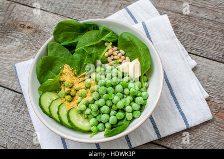 Ingredienti per i piselli spinaci pesto di basilico in una ciotola bianco su uno sfondo di legno. Amore per un sano cibo crudo concetto. Foto Stock