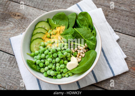 Ingredienti per i piselli spinaci pesto di basilico in una ciotola bianco su uno sfondo di legno. Amore per un sano cibo crudo concetto. Foto Stock