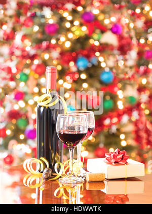Bicchieri di vino, vintage cavatappi, presente e unopen bottiglia di vino sulla tavola di Mahoney con un luminoso albero di Natale luci in background. Formato verticale l Foto Stock