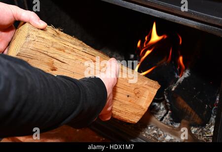 Man mano mettendo il log in al fuoco che arde nel caminetto. L'uomo addensarsi il legno nel camino. Foto Stock