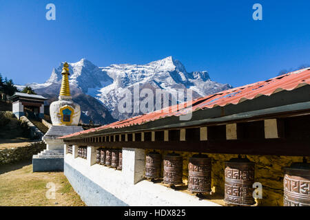 Una fila di preghiera tibetano ruote e un bianco stupa, montagne coperte di neve in lontananza Foto Stock