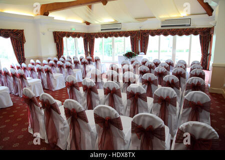 Una camera di cui pronto per un matrimonio civile cerimonia, sedie con i coperchi di colore bianco e legati con rosa scuro archi Foto Stock