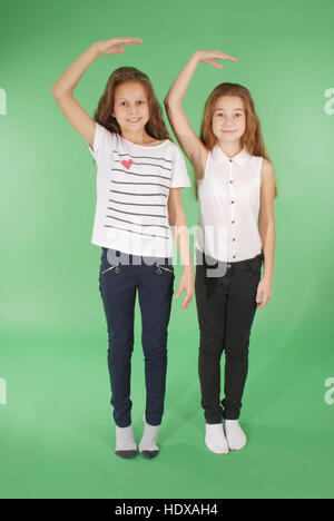 Due ragazze della scuola tenere le mani sopra la testa e misurando la sua crescita isolato su verde Foto Stock