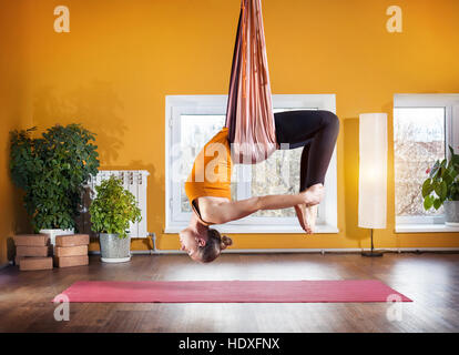 Giovane donna facendo antigravity yoga indietro la posizione di piegatura in studio con pareti di colore giallo Foto Stock