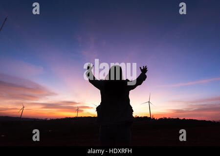 Silhouette donna turistica mano sollevata al tramonto sulla turbina a serbatoio in condizioni di scarsa illuminazione Foto Stock