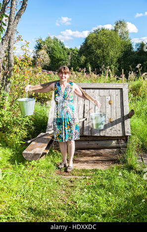 Giovane donna attraente vicino al villaggio di legno e acqua in estate giornata di sole Foto Stock