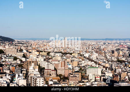 Giappone, Kobe. Il giorno della luna in cielo blu chiaro, visto oltre la città di Kobe. Punto di vista elevato, cityscape, infinite proliferazione urbana. Foto Stock