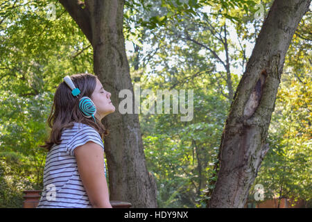 Ragazza ascoltando la musica attraverso le cuffie nel parco Foto Stock