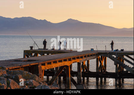 I pescatori del mare nel vecchio molo Portencross al tramonto con le colline di Aran dietro. Foto Stock