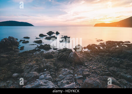 Black Rock Beach con lattiginoso liscia della superficie del mare e del tramonto dietro la montagna sul cielo nuvoloso. Foto Stock