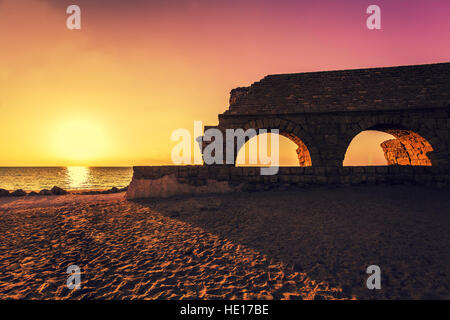 Resti dell'antico acquedotto romano nella città antica Cesarea al tramonto. Israele. Foto Stock