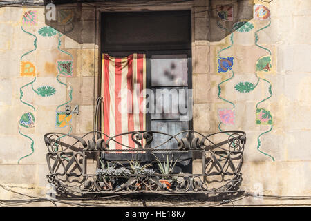 Un balcone a Barcellona Spagna con bandiera catalana visualizzato, elaborare elementi in ferro battuto e fiori policrome dipinte sulla facciata dell'edificio. Foto Stock