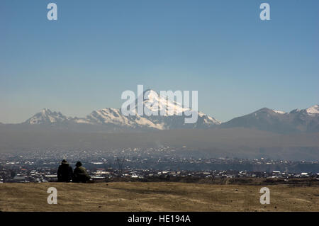 Due uomini, volti non visibile, sedersi in un posto di potenza, apacheta, vicino a La Paz, Bolivia, con vista del Illimani innevato picco di montagna Foto Stock