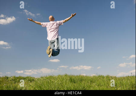 Giovane uomo salti intorno in un prato con bracci outstreched Foto Stock