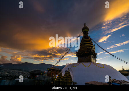 Il bianco stupa di swayambhunath temple, Monkey Temple, è decorata con la preghiera tibetano bandiere, big arancione tramonto sopra le nuvole Foto Stock