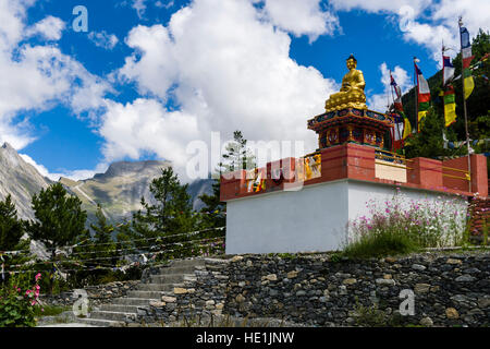 Un Dorato statua del Buddha è impostata su un basamento in pietra, circondato da bandiere di preghiera Foto Stock