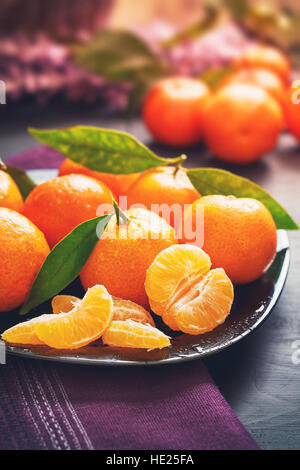 Clementine fresche con foglie servita su piastra, su tavoli in legno nero Foto Stock