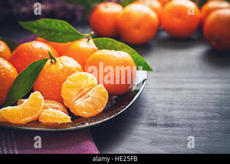 Clementine fresche con foglie servita su piastra, su tavoli in legno nero. Spazio di copia Foto Stock