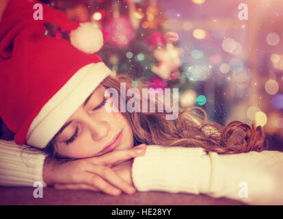 Closeup ritratto di una bella ragazza in attesa di regali di Natale, stanco bambino indossando Santa Red Hat che dorme nella camera decorata a casa Foto Stock