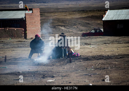 Un giovane boliviani, volti oscurato dal fumo e ombra, sedersi accanto a un ardente mesa, un agosto che offre alla Pachamama Foto Stock