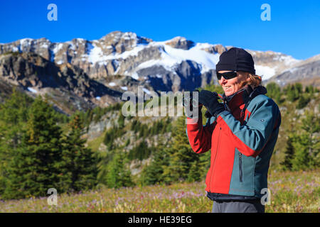 Una femmina di escursionista usando il binocolo per visualizzare la fauna selvatica a Healy Pass nel Parco Nazionale di Banff nelle Montagne Rocciose Canadesi Alberta Canada Foto Stock