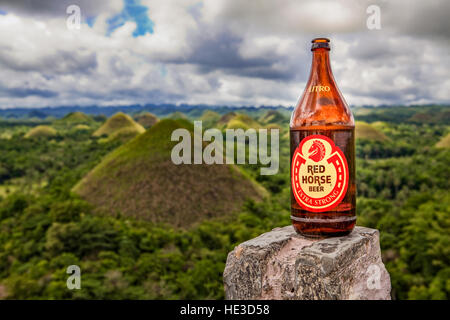 Una bottiglia da un litro di cavallo rosso Ale sorge su una roccia con il cioccolato colline di Bohol in background, Filippine. Foto Stock