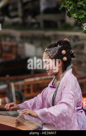 Giovane donna ragazza in abito tradizionale la riproduzione del Guzhengin strumenti musicali in acqua il villaggio di Tongli, Cina. Foto Stock