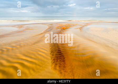 La torba acqua colorata che fluisce oltre Traigh Garraidh (Garry spiaggia) da Tolsta sul rivestimento est dell isola di Lewis, Ebridi Esterne, Scotland, Regno Unito Foto Stock