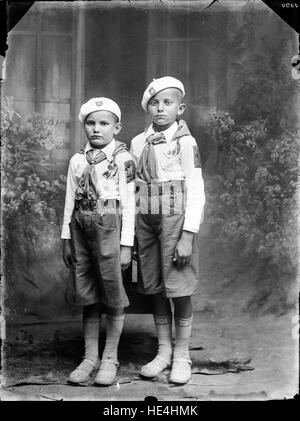 Una fotografia in bianco e nero di due bambini vestiti in uniforme da guardia, scattata da Costica Acsinte a Ialomita, Romania. Scattata su un piatto di vetro, questa immagine dell'inizio del XX secolo offre uno sguardo sulla vita dell'infanzia e sull'abbigliamento storico nella Romania rurale durante il periodo. Foto Stock
