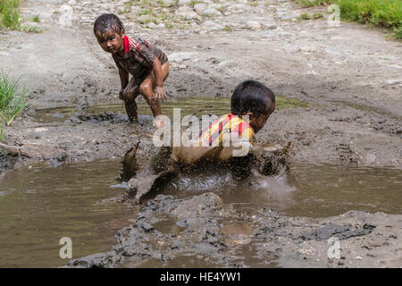 Due ragazzi locali, solo indossare camicie, stanno giocando nel fango di un fiume Foto Stock