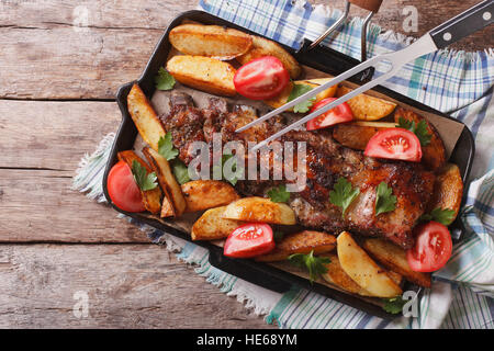 Costolette di Maiale con patate al forno e pomodori in una padella di close-up. vista orizzontale dal di sopra Foto Stock