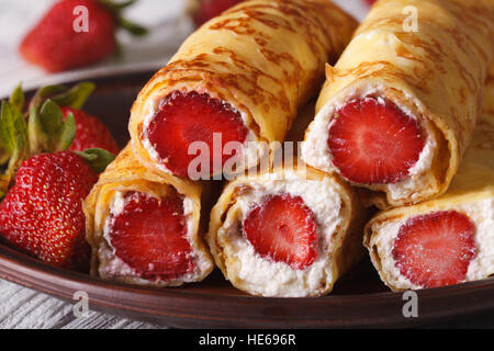 Rulli con fragole fresche e crema di formaggio su una piastra macro. orizzontale Foto Stock