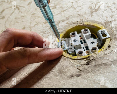 Mano che tiene un cacciavite punta verso un danneggiata presa elettrica. Foto Stock