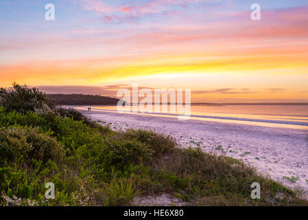 Sunrise e due persone lontane che camminano a Callala Bay sulla costa sud del nuovo Galles del Sud in Australia Foto Stock