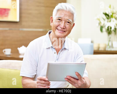 Senior asian uomo seduto sul divano tenendo un computer tablet guardando la telecamera sorridendo. Foto Stock