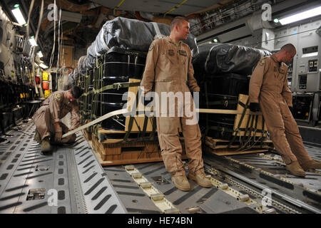 Stati Uniti Air Force loadmaster Senior Airman Josh Faust, sinistra, fascette contenitore sistema di consegna fasci per il pavimento di un C-17 Globemaster III, mentre il personale loadmaster Sgt. Gabriel risme, centro, e pilota Capt. Dave Goodale tenere i fasci in luogo a Kandahar Airfield, Afghanistan, 27 maggio 2010. L'equipaggio liberato i fasci oltre l'Afghanistan, il rifornimento della Combined Joint Special Operations Task Force con cibo e acqua e carburante. Goodale, risme e Faust sono assegnati alla 816th Airlift Expeditionary Squadron. Foto Stock