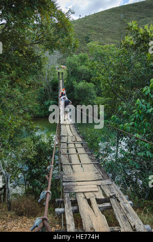 Un gruppo di turisti attraversare un ponte di legno in disrepair sospesi da funi metalliche oltre il Sao Francisco fiume in Brasile. Foto Stock