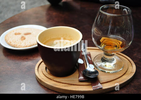 In ceramica scura tazza di caffè, un bicchiere di cognac e italiana mandorla cantuccini cookie su una piastra bianca su un vecchio tavolo di legno al cafe Foto Stock